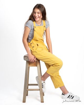 Girl in yellow overalls laughs away from the camera at a Melbourne family portrait studio