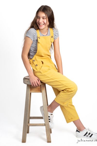 Girl in yellow overalls laughs away from the camera at a Melbourne family portrait studio